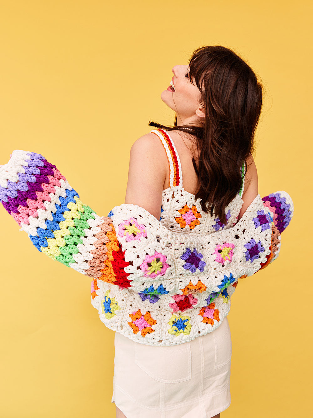 Woman with dark wavy hair wears a colourful granny square crocheted cardigan from Cardigang.