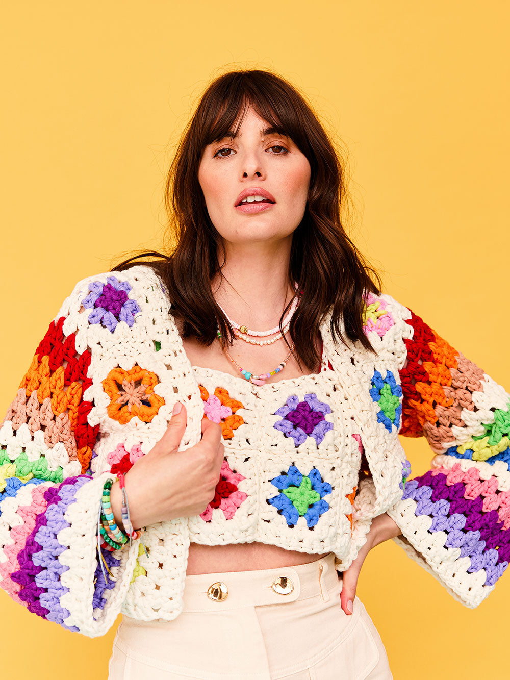 Woman with dark wavy hair wears a colourful granny square crocheted cardigan from Cardigang.