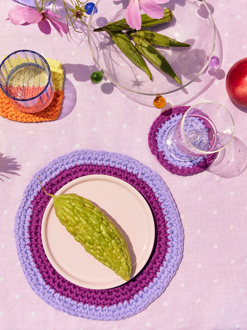 Isla plum and lilac circular crochet placemats and coasters styled on a table with vegetables and glassware. 