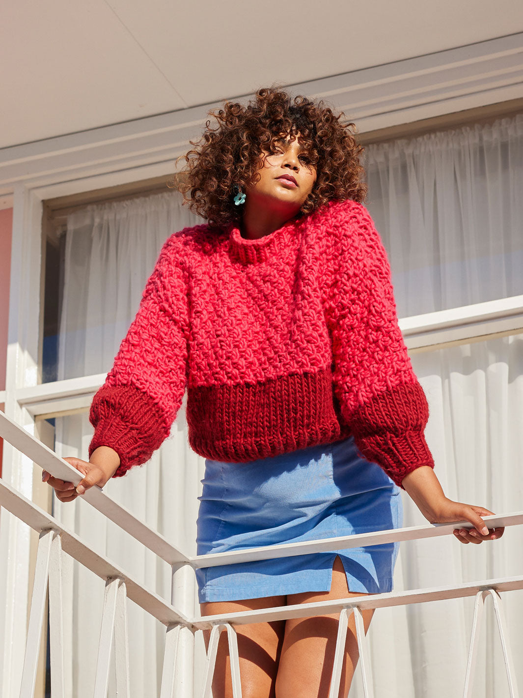 Girl stands over balcony wearing a skirt and chunky knitted Cardigang jumper