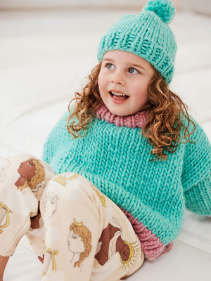 Little girl with curly hair wears a green beanie and matching green and pink jumper