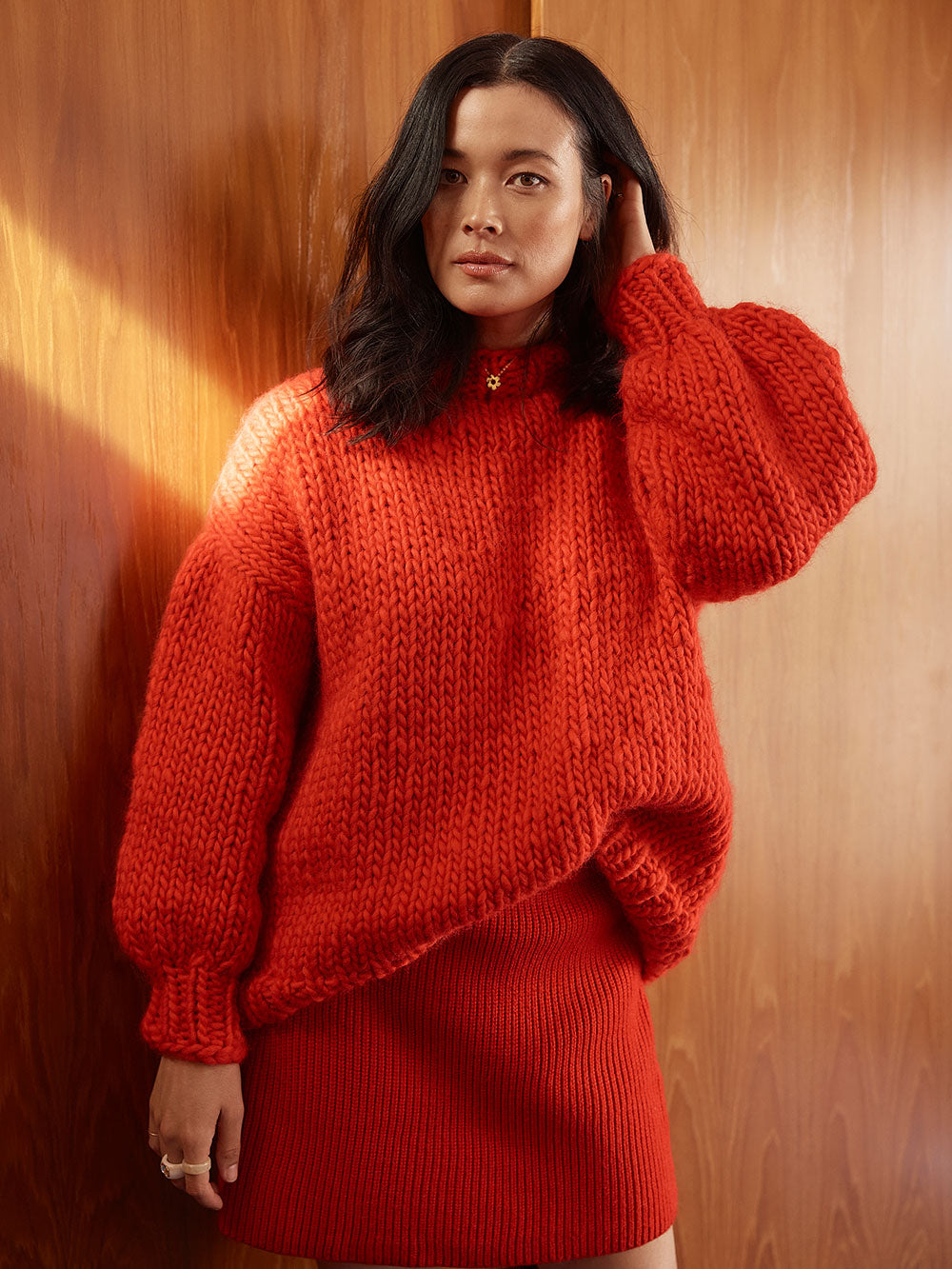 Woman standing in front of wardrobe wears a bright red chunky knitted jumper and red skirt