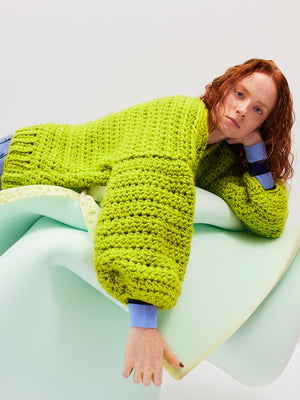 Female with long wavy red hair is wearing a chartreuse green chunky hand crocheted woollen cardigan