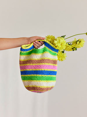 Photograph of person holding a brightly coloured stripey crochet bucket bag spilling with flowers