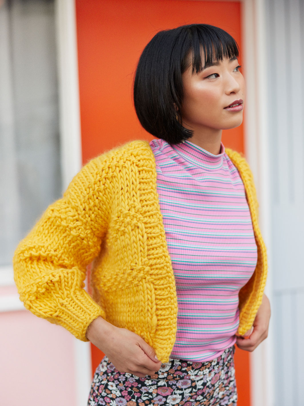 Woman in pink stripey tshirt wears a chunky knitted yellow cardigan