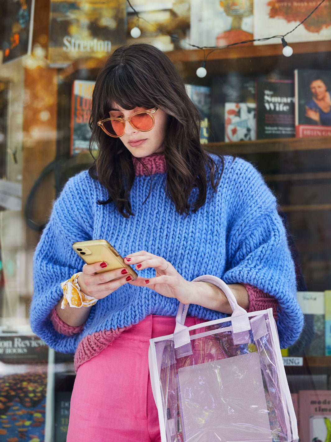 Girl looking at iphone wearing a chunky knitted blue jumper with pink ribbing