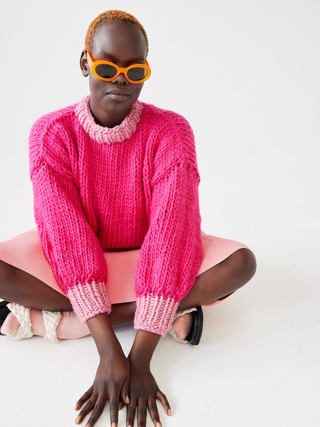 Girl sitting on the floor wearing sunglasses and chunky knitted bright pink jumper