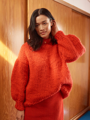 Woman standing in front of wardrobe wears a bright red chunky knitted jumper and red skirt