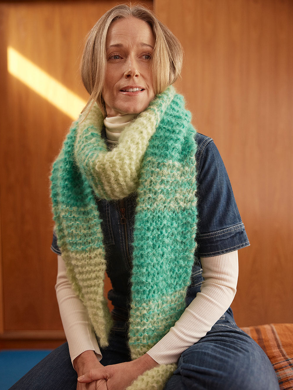 Woman sits on bed wearing a hand knitted mohair scarf