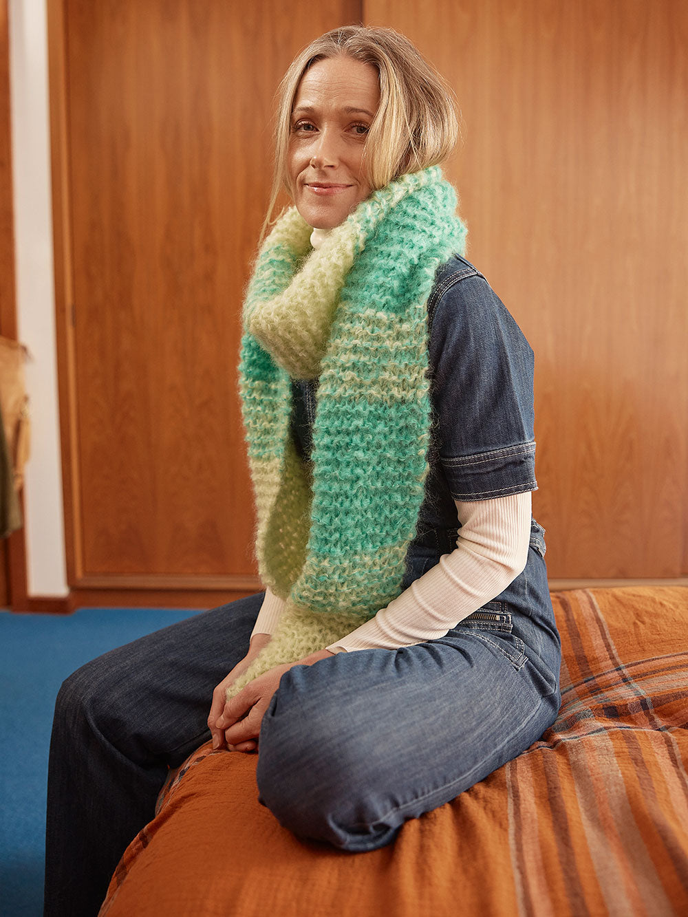 Woman sits in front of closet wearing a hand knitted mohair scarf
