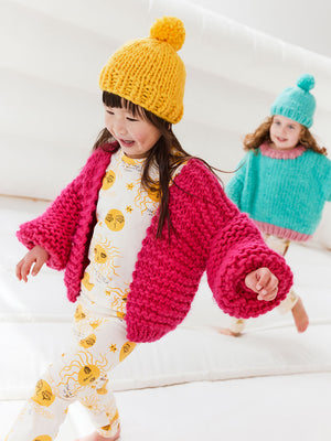 little girl is running on a white jumping castle wearing a yellow beanie, chunky knitted pink cardigan and a matching tshirt and leggings