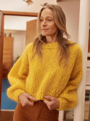 Woman smiles at camera wearing a bright yellow chunky knitted mohair jumper and brown cord jeans. 