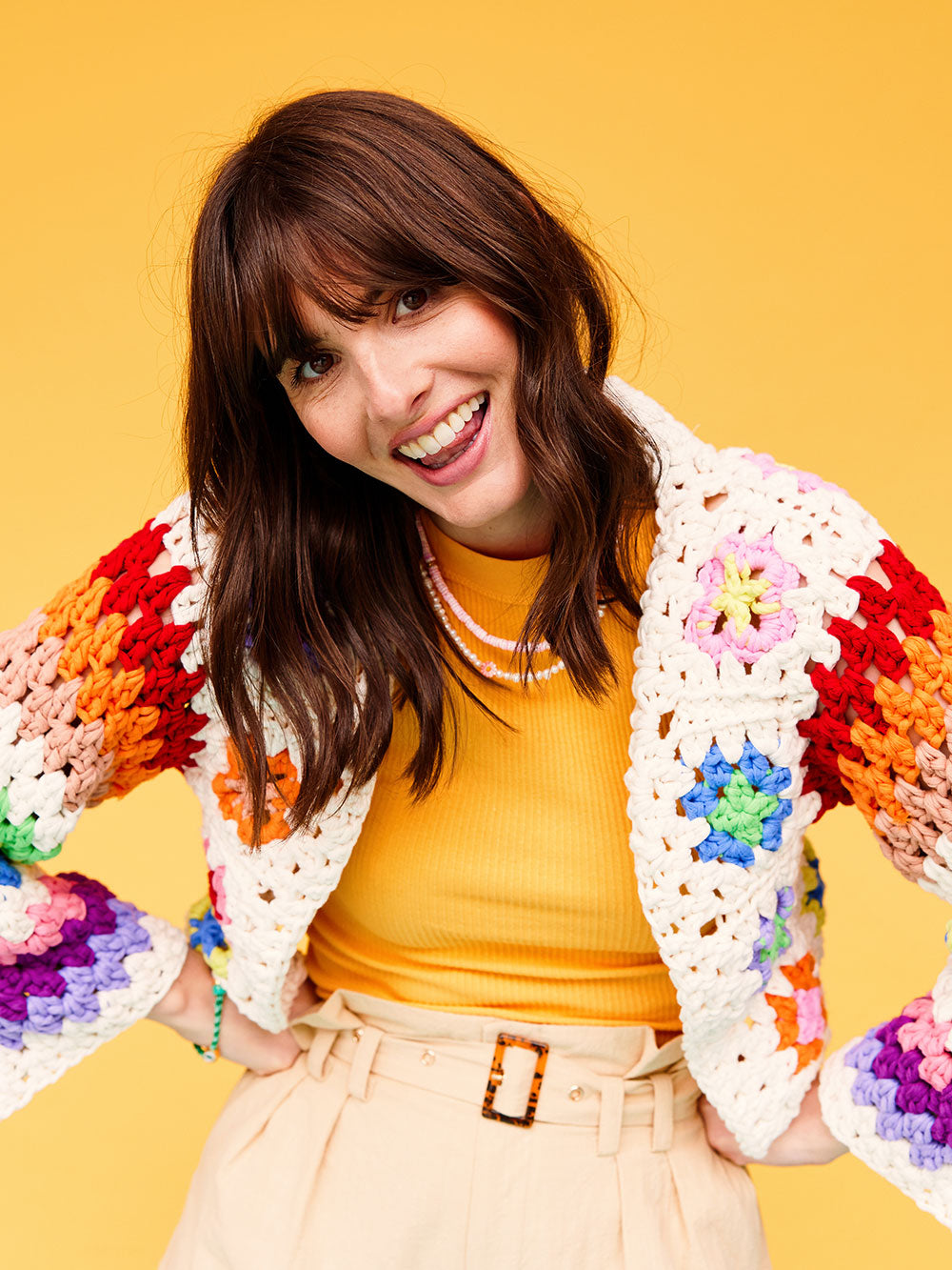Woman with dark wavy hair wears a colourful granny square crocheted cardigan from Cardigang. 