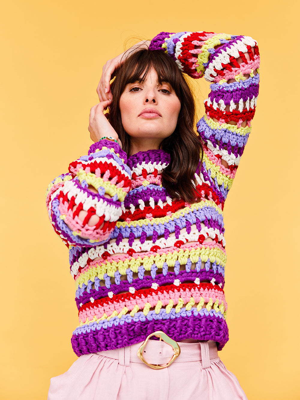 Woman with dark wavy hair is sitting on a lilac stool wearing a DIY striped crochet jumper by Cardigang