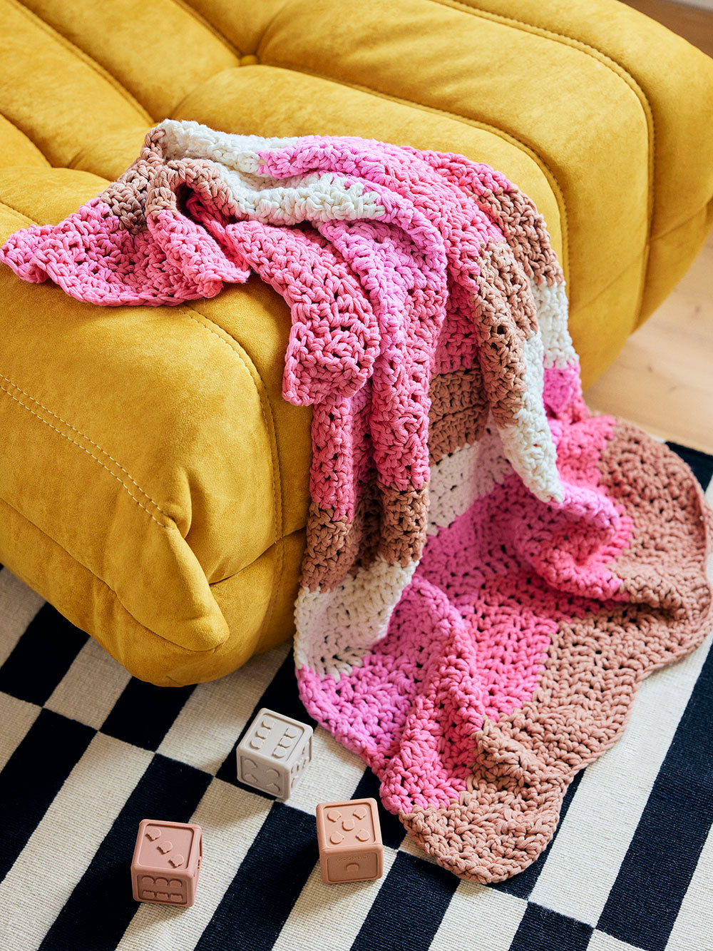Image of Margot wave crochet baby blanket draped over a yellow ottoman.