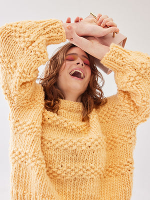 Woman laughing holds hands to forehead. She is wearing a yellow chunky knitted jumper