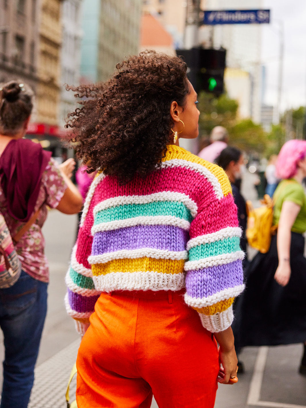 Woman walks away from camera wearing orange pants and a bright colourful knitted jumper