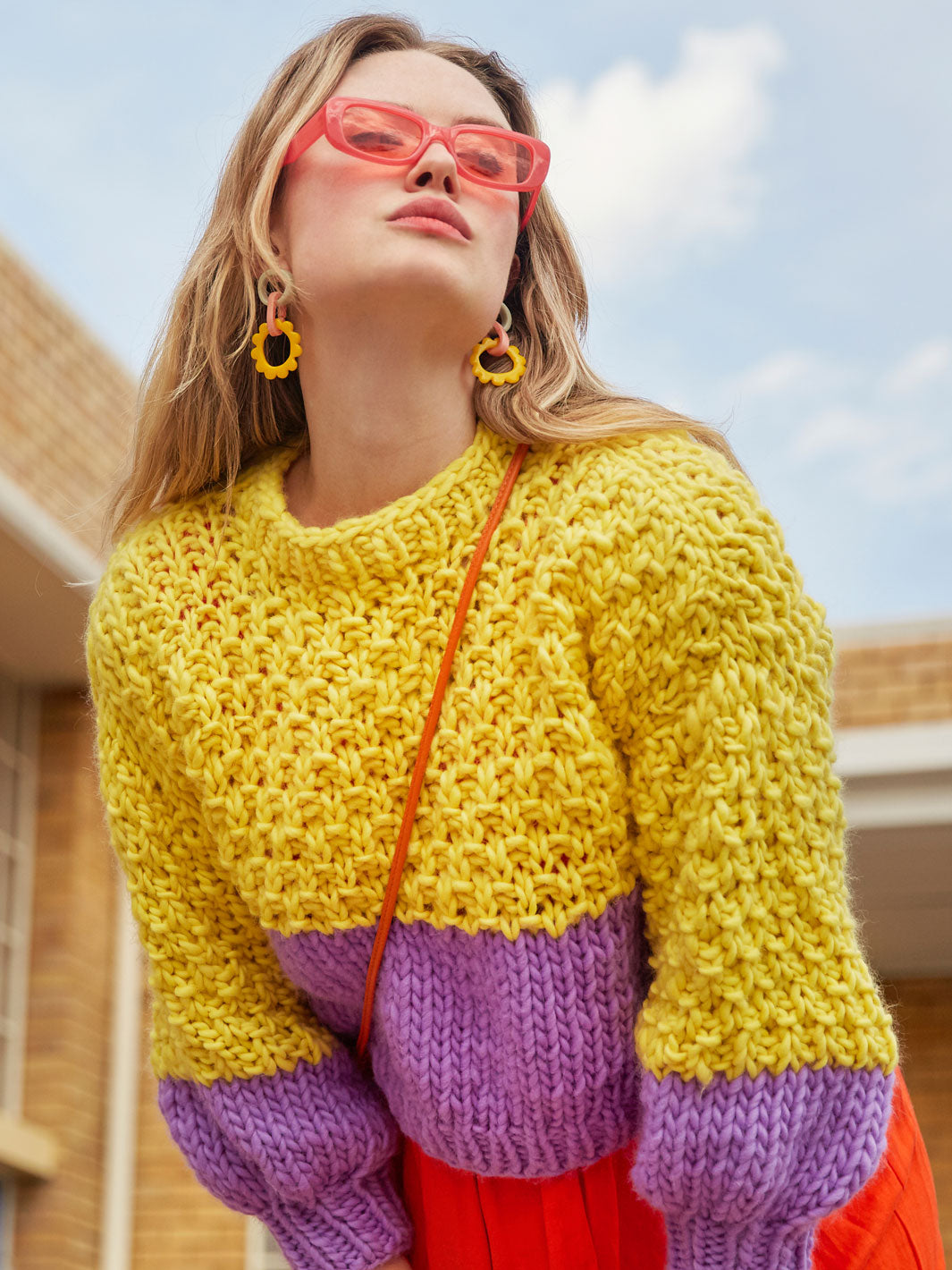 Girl wearing sunglasses leans over in her chunky knitted bright colour jumper