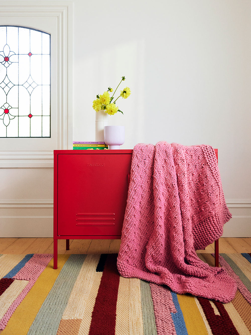 Photo of a dusty pink chunky knitted blanket draped over a red locker.