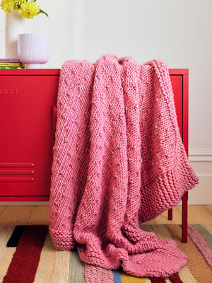 Close up photo of a dusty pink chunky knitted blanket draped over a red locker.