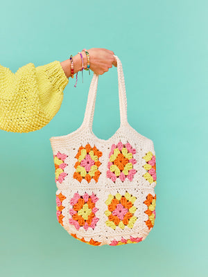 Woman with yellow jumper holds a white crochet Granny Square shopping bag