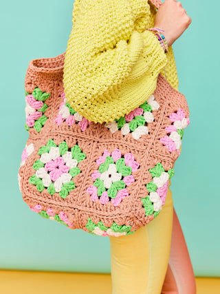 Woman with yellow jumper holds a crochet Granny Square shopping bag