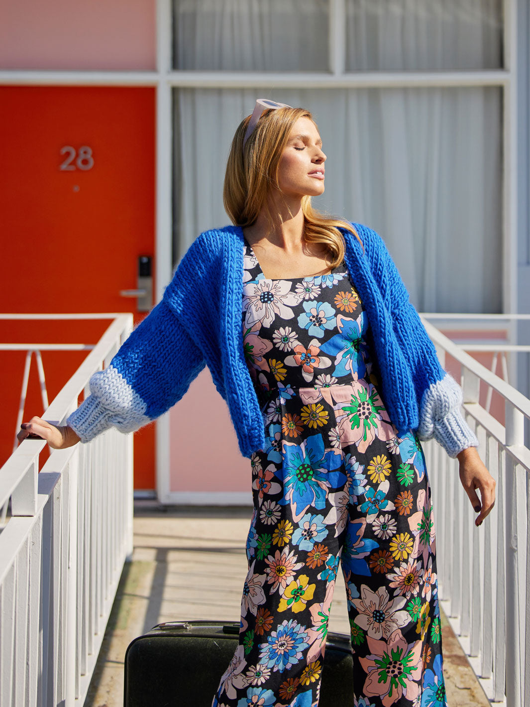 Girls stands in motel wearing floral jumpsuit and blue cardigan