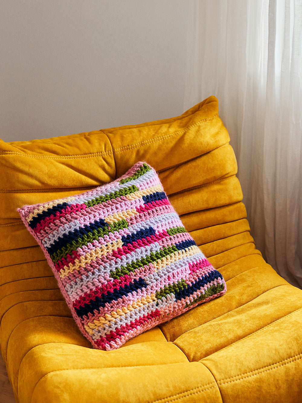 Photo of a chunky crocheted cushion laying on a yellow suede couch