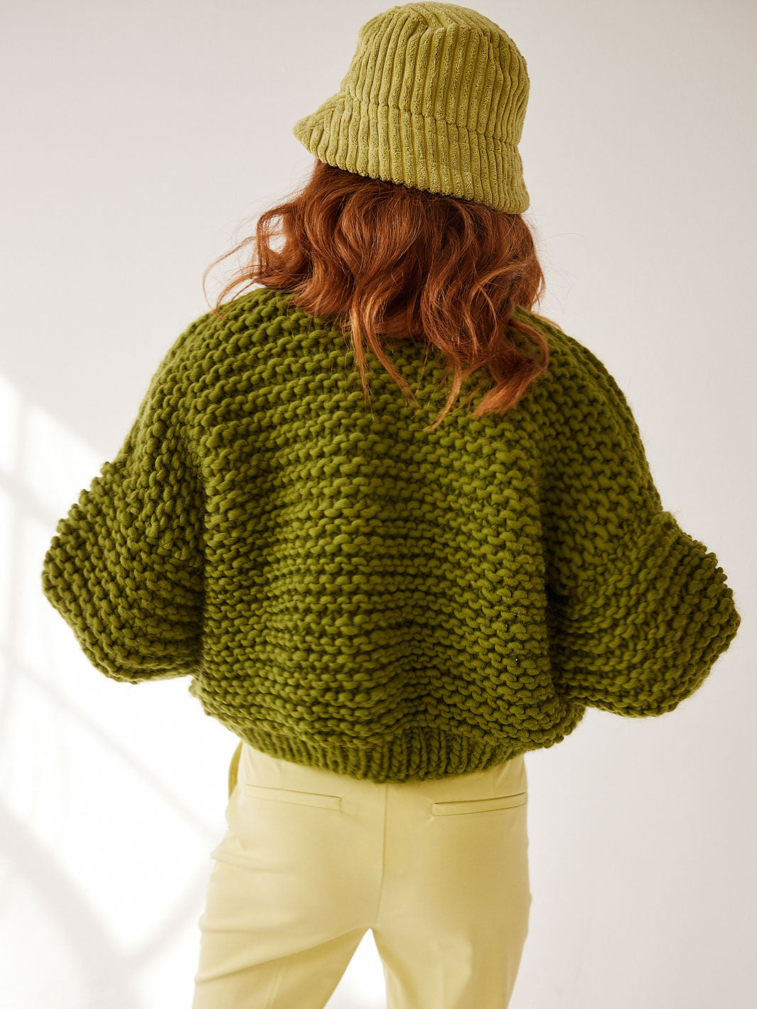 Girl stands with her back to the camera wearing a chunky knitted green cardigan